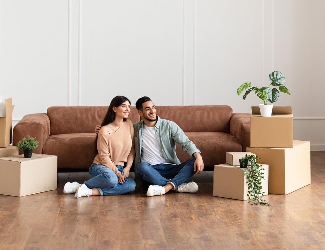 Couple in new home sitting on living room floor with boxes around them