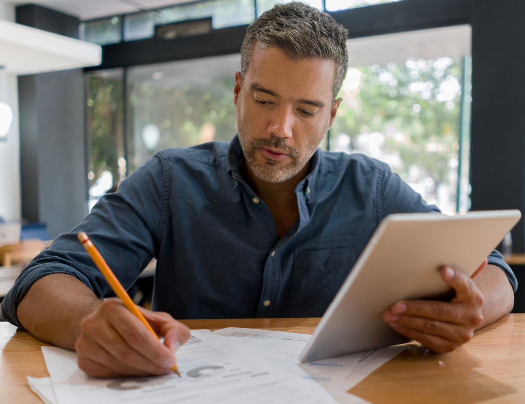 Man in cafe writing and using tablet