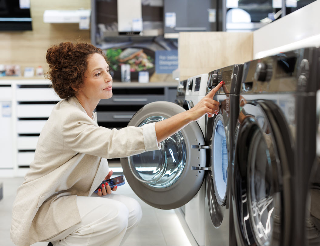 Woman bending down, looking at the inside of a washing machine
