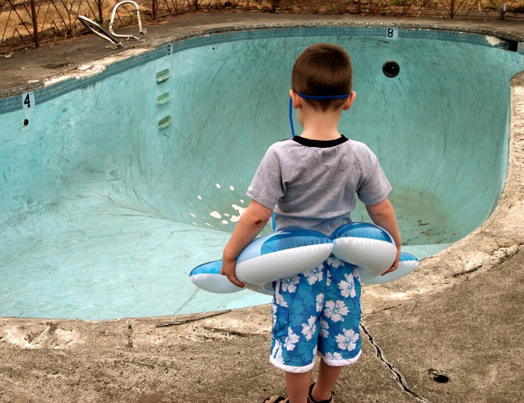 small boy staring at an empty swimming pool