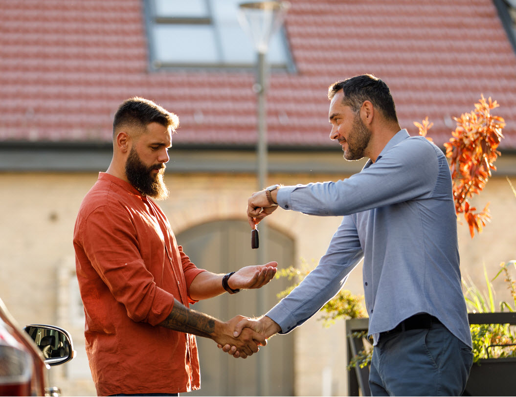 Two men shaking hands and exchanging car keys for a used car purchase