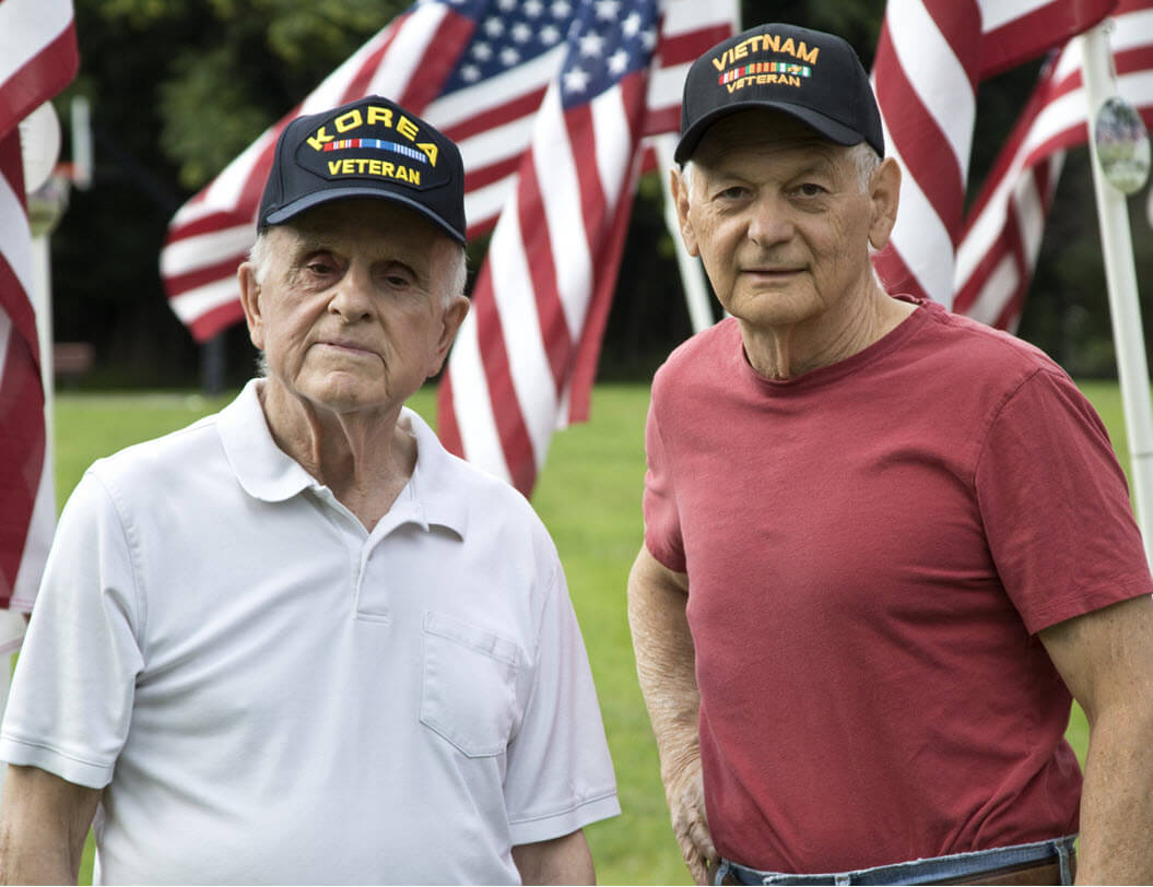 Two Veterans standing in front of American flags
