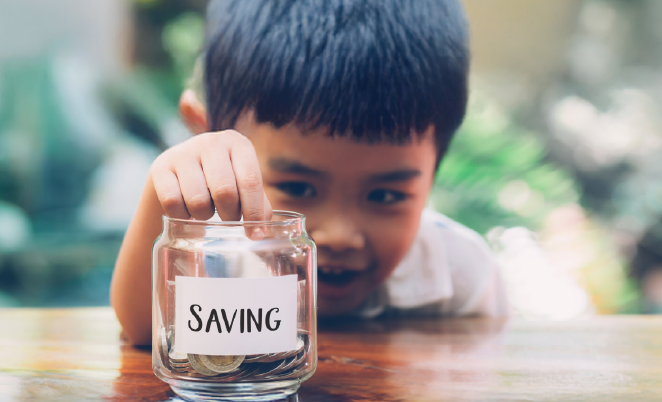 Boy putting money in a jar that is labeled Savings