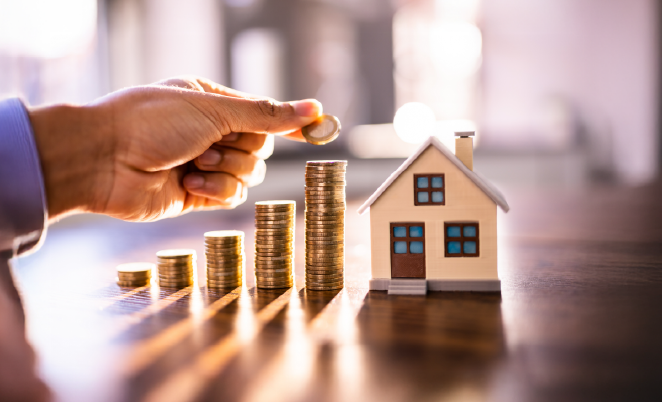 stacks of coins next to a small house replica