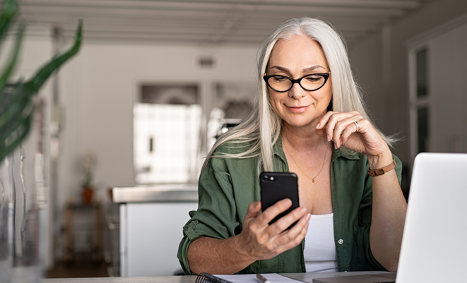 Woman sitting at a laptop while also using her mobile phone