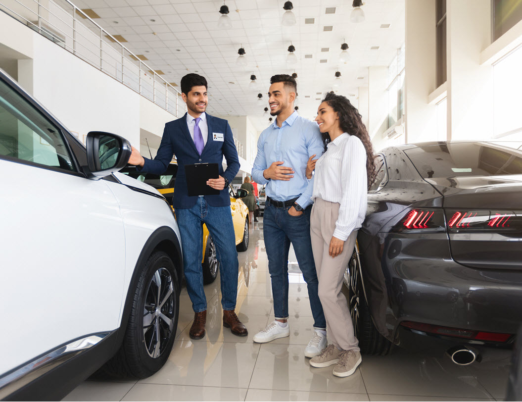 young couple in a car showroom speaking with a male sales person